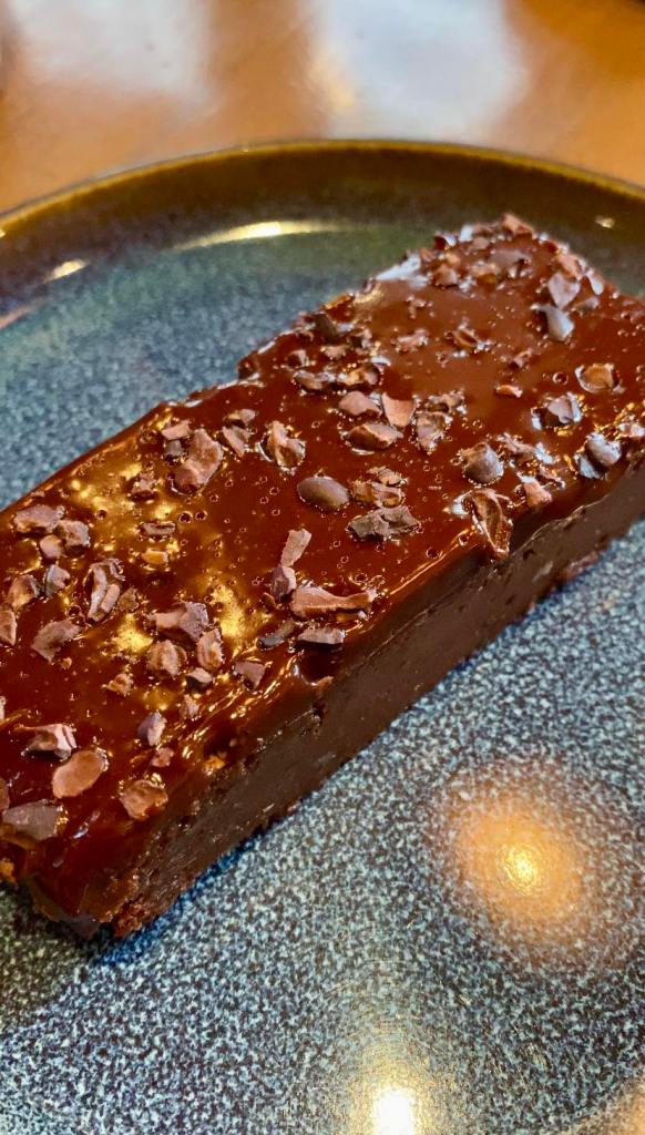 a slice of chocolate fudge brownie with a shiny glaze and chocolate bits on top